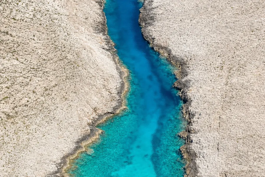 Aerial view of a channel between two rocky islands, the shallow water shading turquoise to deep blue.