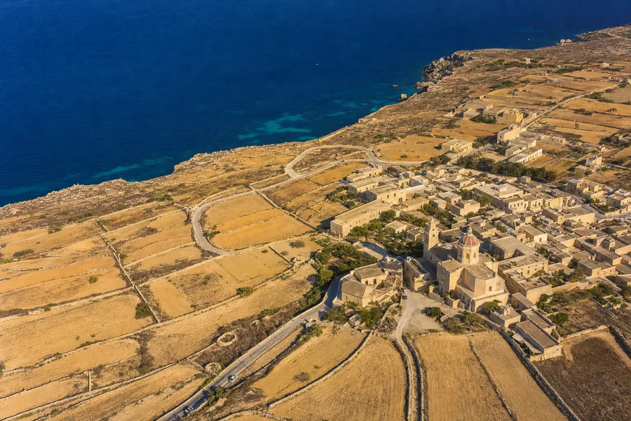 Aerial view of a patchwork of fields and dry stone walls with a winding road between villages.
