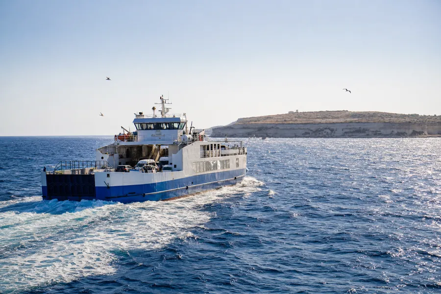 A passenger ferry crossing open blue water towards low limestone cliffs.